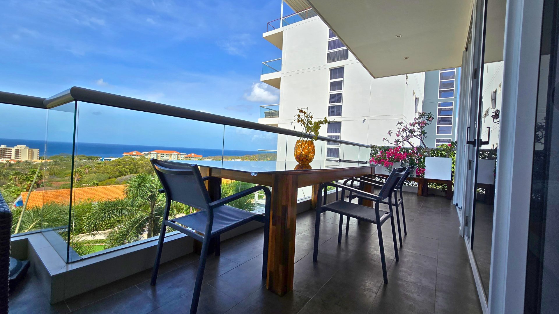 Terrace dining table for four with glass balustrade and a sweeping view over palm trees to the Caribbean Sea